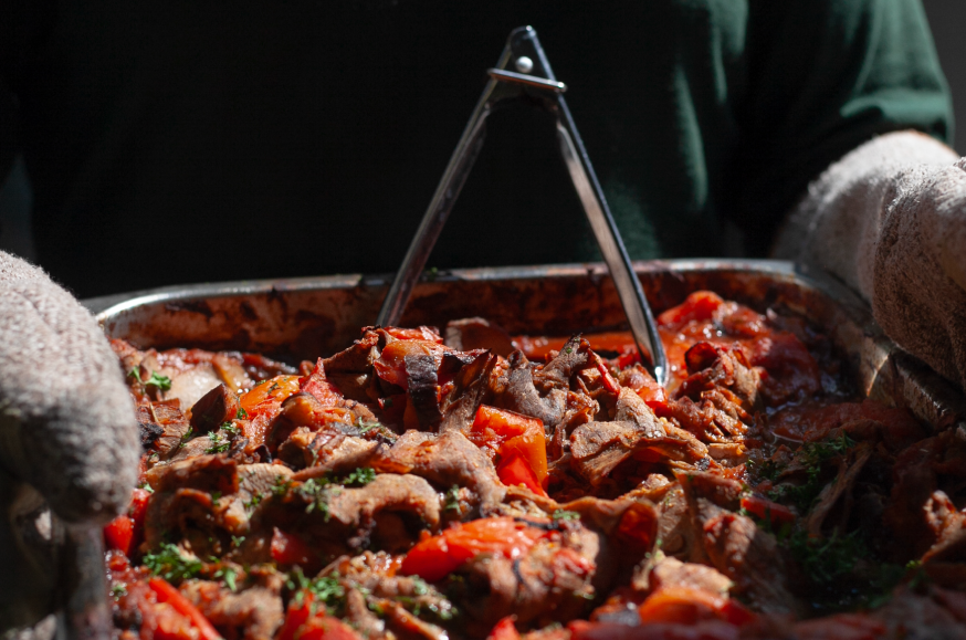 TheGatheringPlace_Food_V1 A volunteer holding a large tray of beef and tomato casserole.